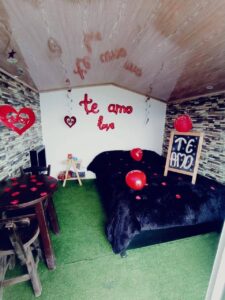 Cabaña de glamping con una decoración romántica que incluye corazones, velas y un letrero de "Te amo", perfecta para planes románticos de glamping